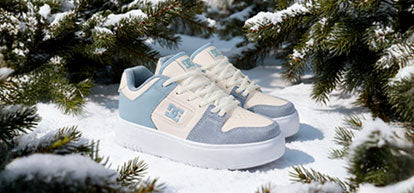 Blue and white sneakers on a snowy ground with pine branches.