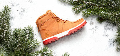 Orange winter boot with red sole on a snowy background with pine branches