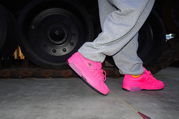 Person wearing bright pink sneakers and gray sweatpants standing on a concrete floor with a vehicle in the background.