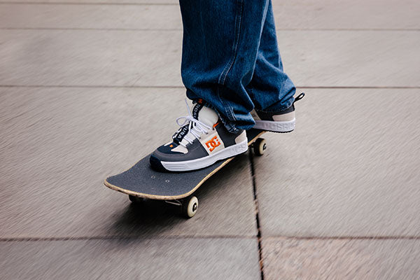 Person skateboarding in navy and white sneakers with an orange DC logo on a concrete surface