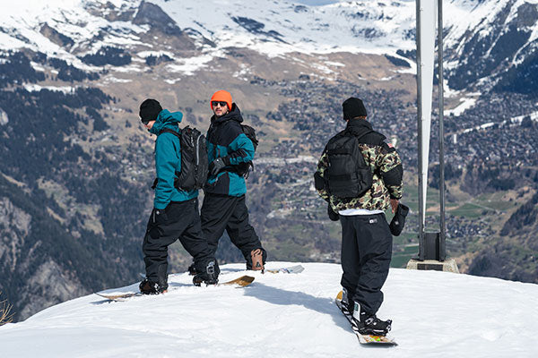 Three snowboarders on a snowy mountain with a scenic view of mountains and valleys.