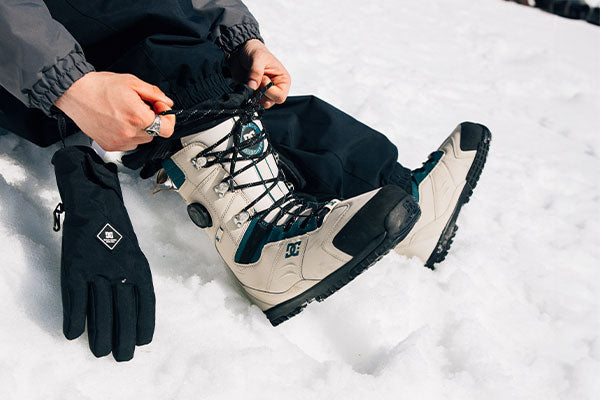 Person adjusting hiking boot in the snow with a focus on winter gear.