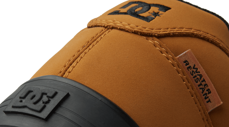 Close-up of a brown boot with black sole and brand logo on a green background